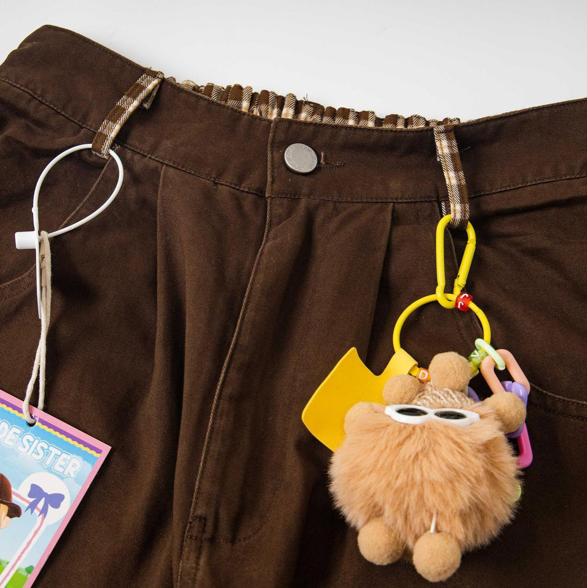 Cartoon embroidered patchwork jeans in brown with plaid waistband and colorful keychain accessory