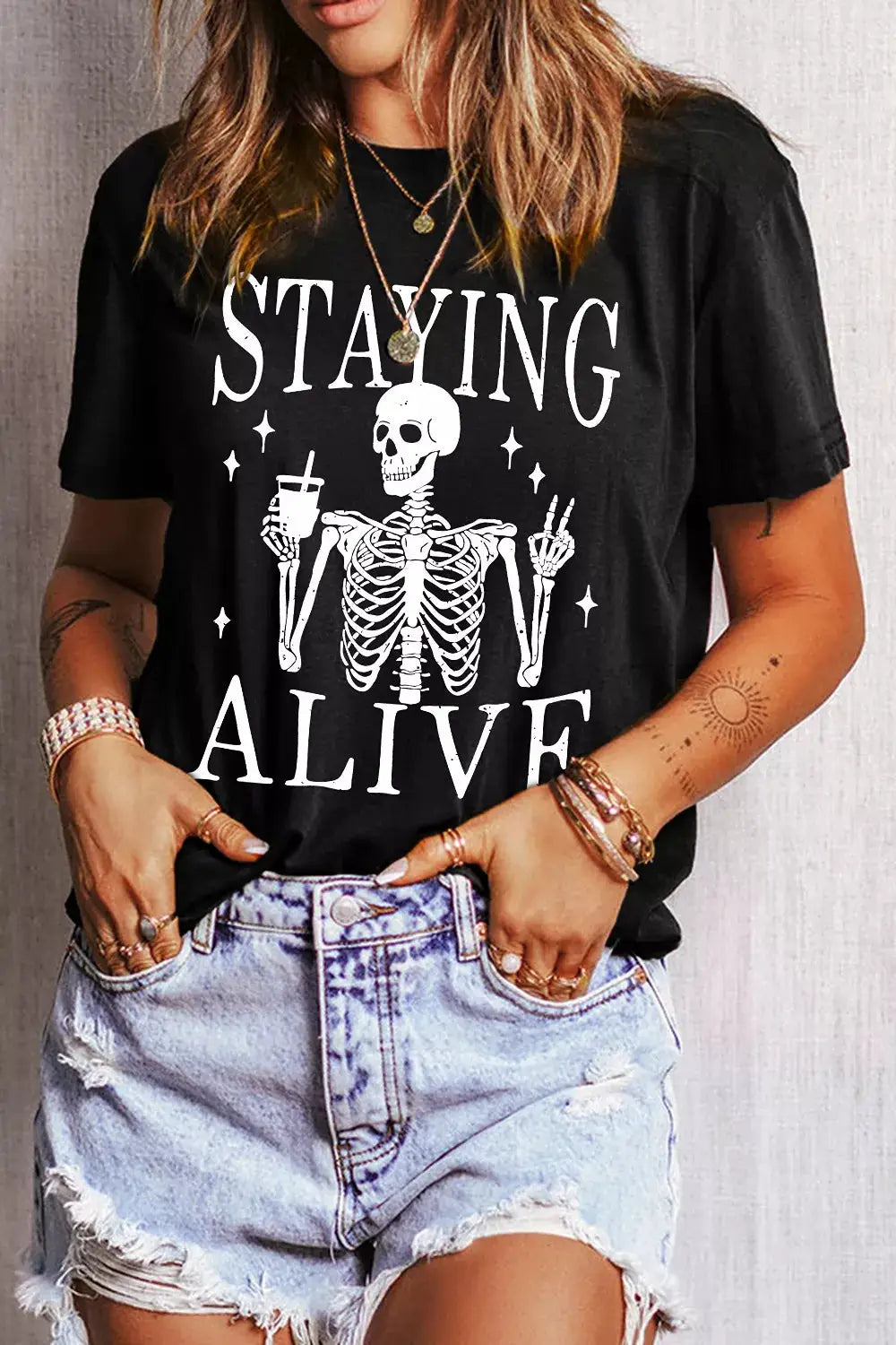 STAYING ALIVE black round-neck T-shirt with white skeleton graphic holding a drink