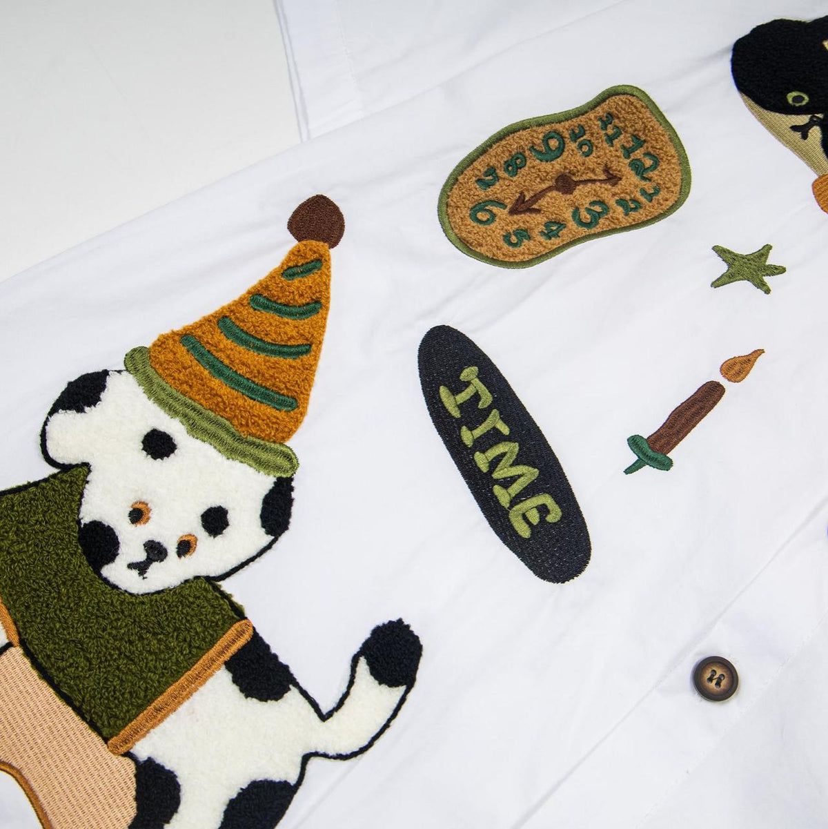 Spotted puppy cat embroidered short sleeved shirt on white fabric with a dog wearing an orange party hat