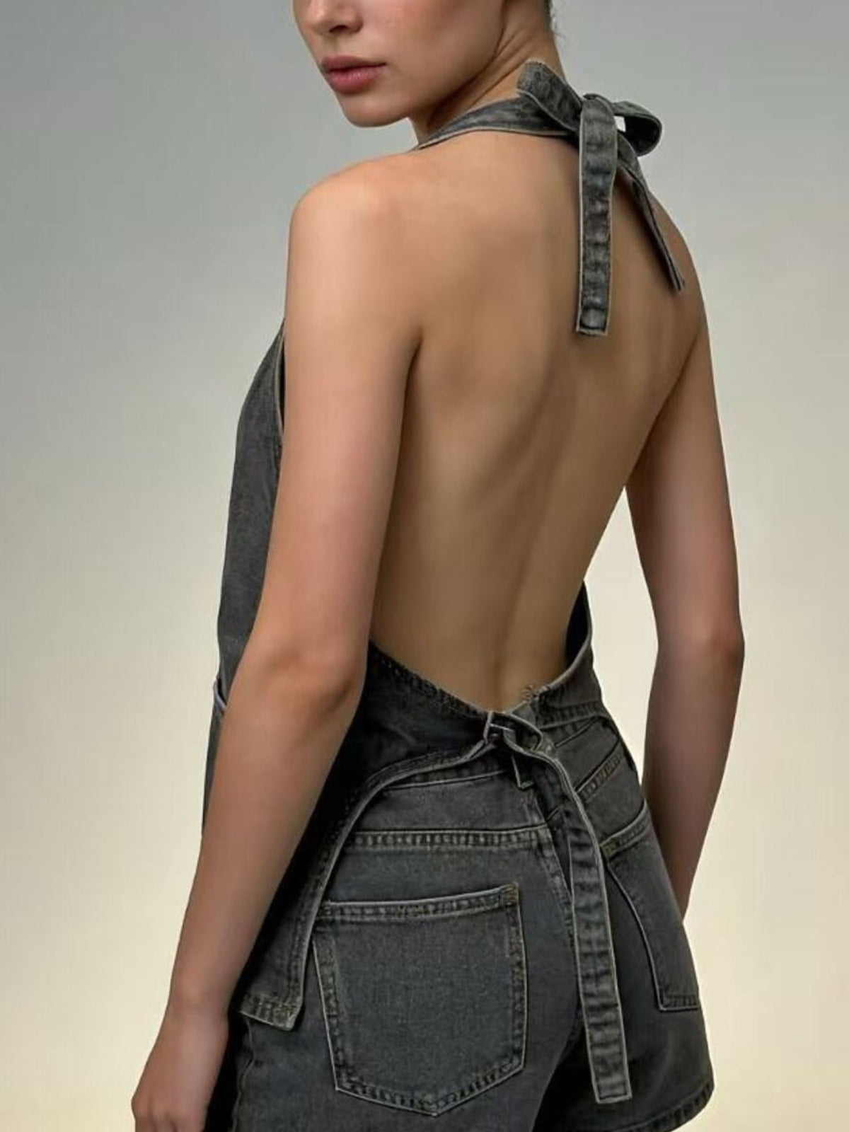 Halter neck denim vest with adjustable tie closure in gray wash; back view.