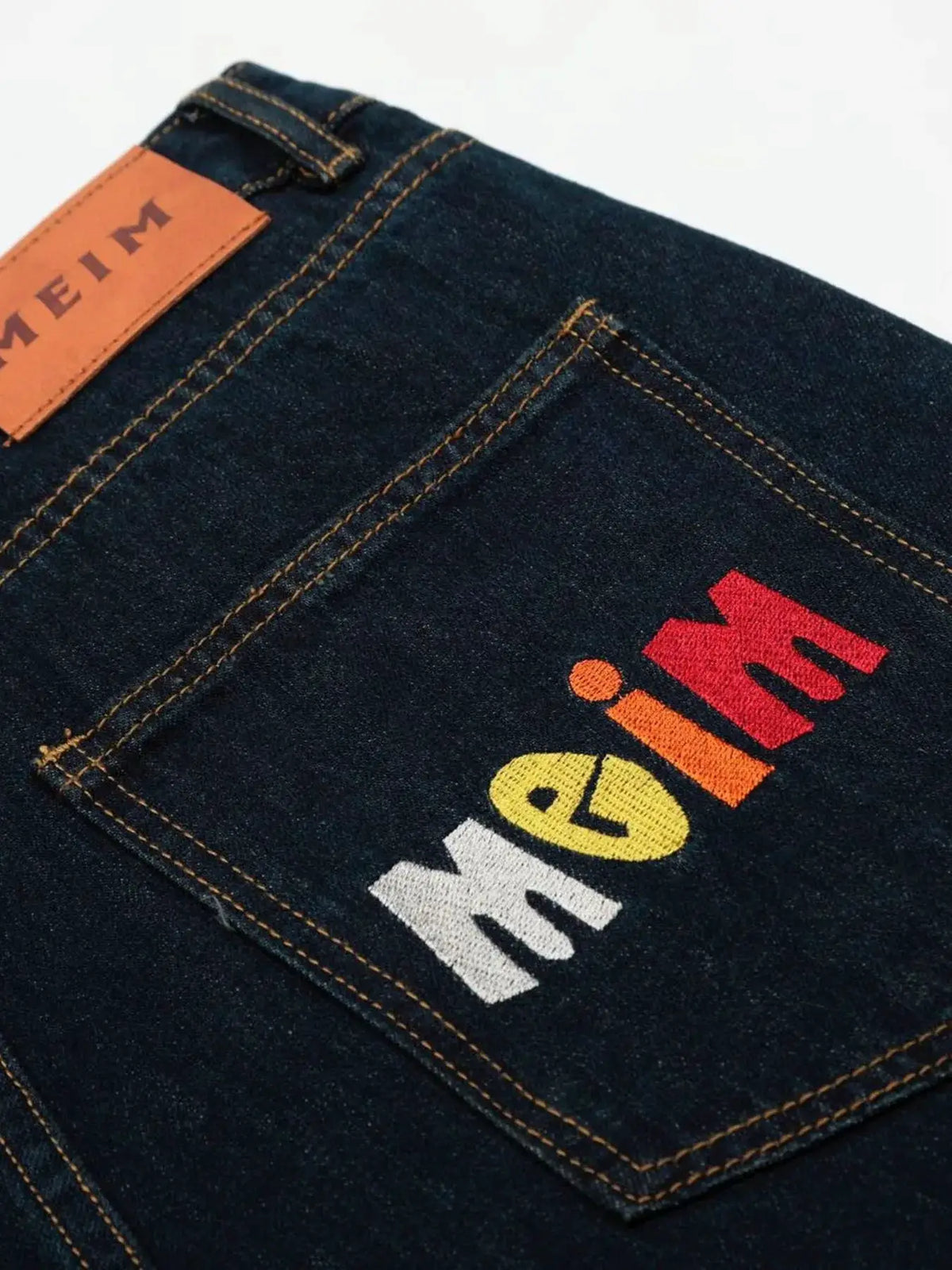 Oversized men's wide-leg denim shorts, 100% cotton, dark indigo with orange stitching and multicolor graphic on pocket