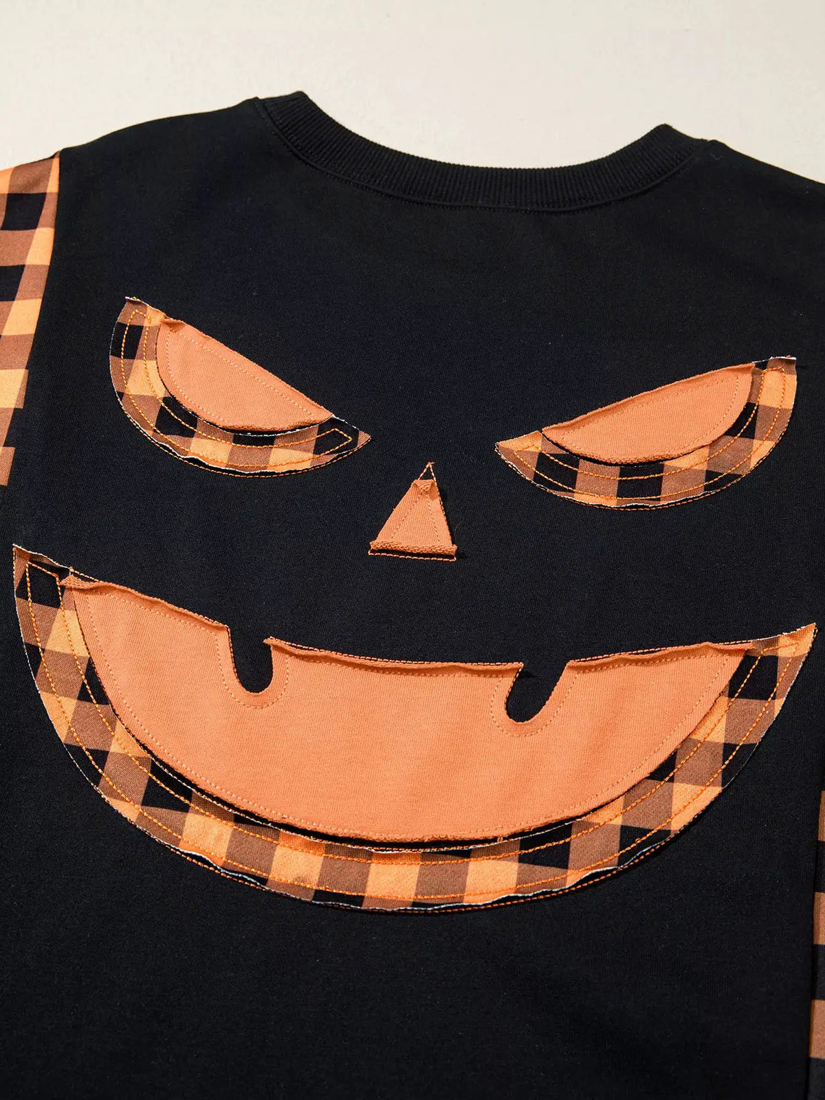Patchwork plaid pumpkin face long-sleeve top; black knit with orange plaid appliqué accents