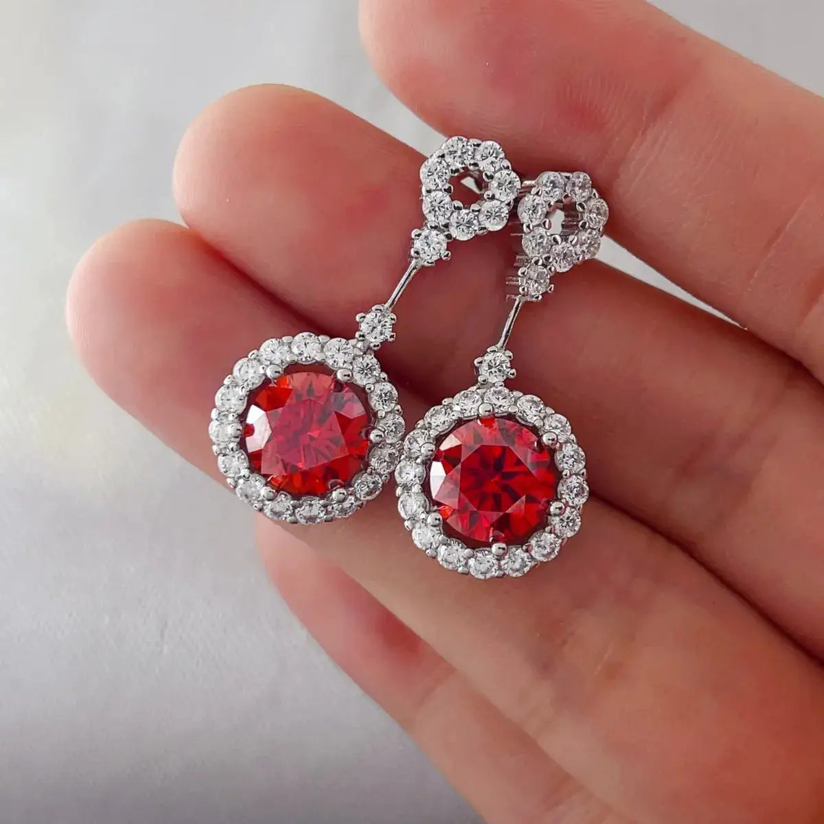 Pair of ruby red crystal drop earrings with rhinestone halo in silver-tone.