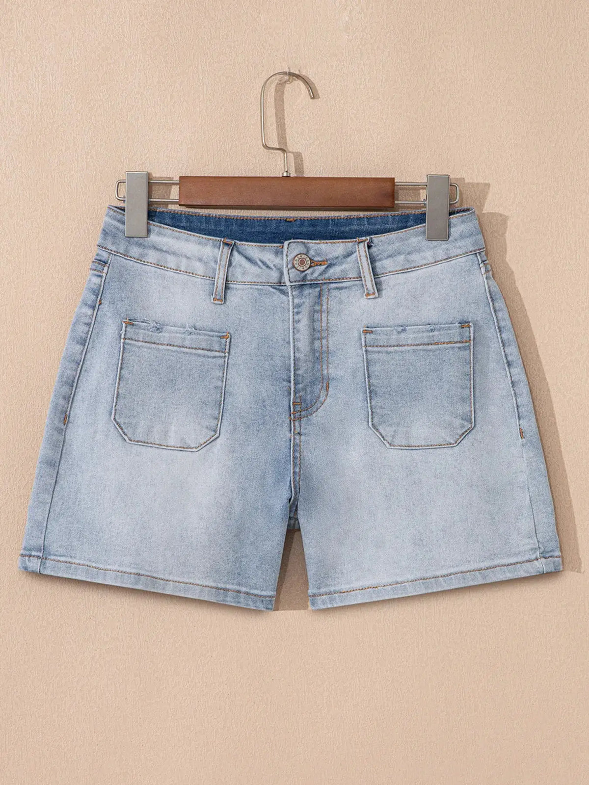 Wash High Rise Denim Shorts in light blue wash with back pockets, hanging on a wooden hanger