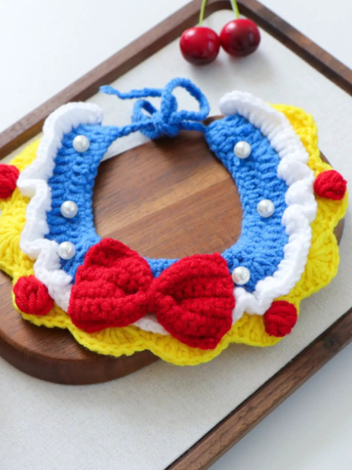 Contrast Pet Scarf crochet collar in blue with white trim, pearl beads, yellow edge, and red pom-poms.