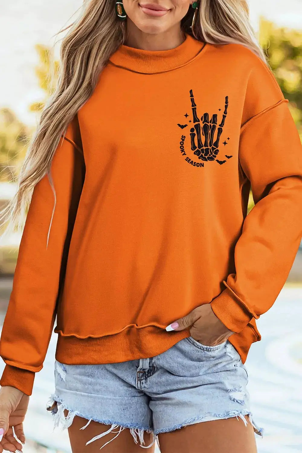 Spooky Season mock-neck reversible Halloween sweatshirt in orange with black skeleton hand and bat graphic.