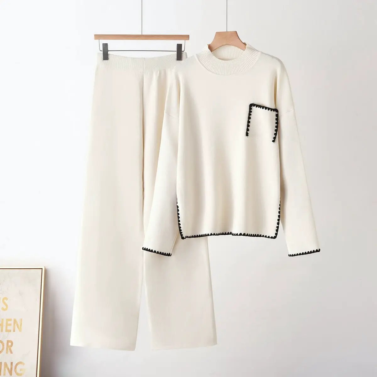 Two-piece knit set in cream with half-high neck top and straight-leg pants, black whipstitch trim on pocket and hems