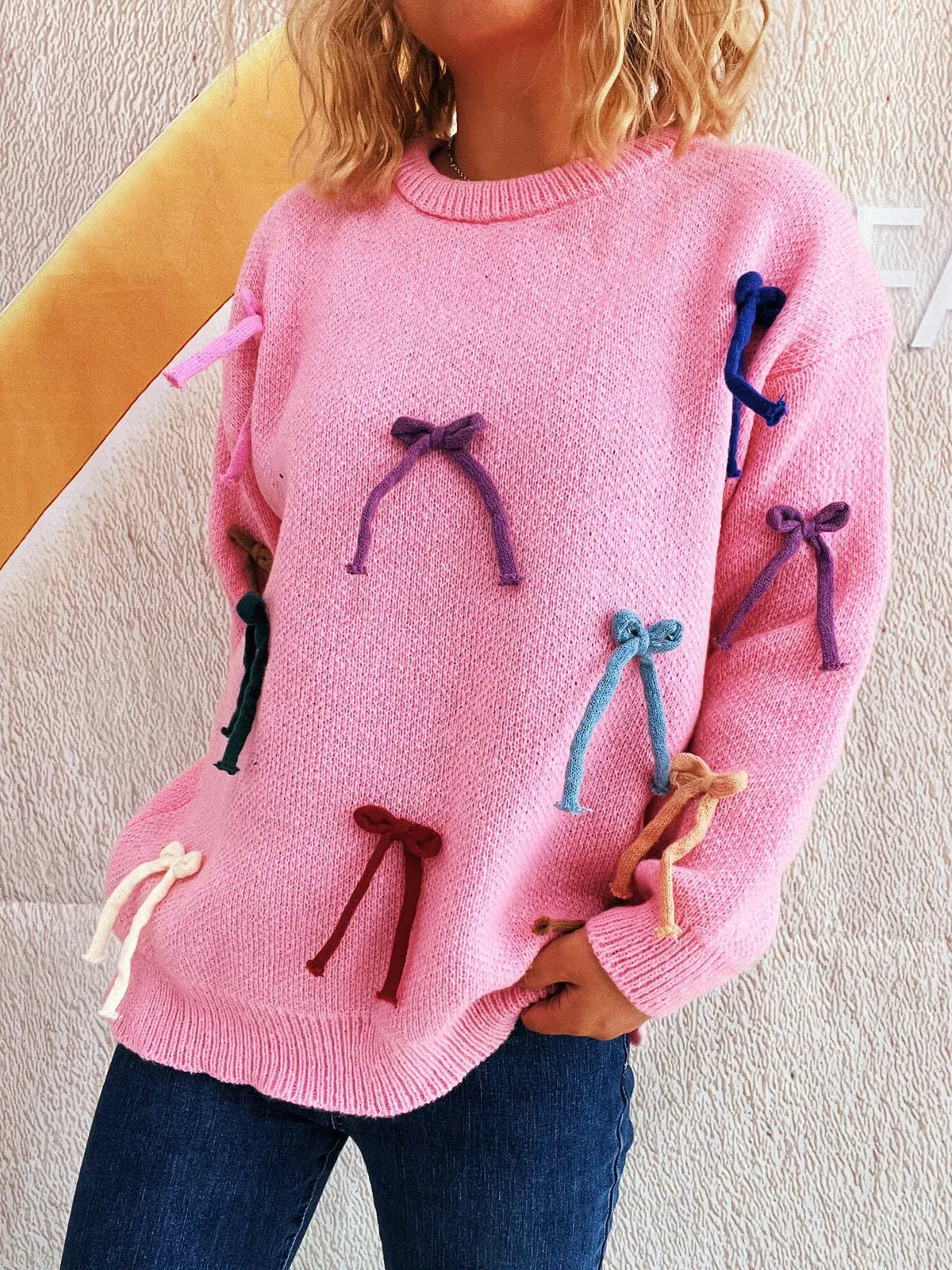 Vibrant pink bow-accent round-neck sweater for women with multicolor knit bows along sleeves and front