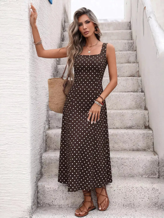 Polka dot sleeveless maxi dress in brown with white dots; worn with a straw tote and sandals