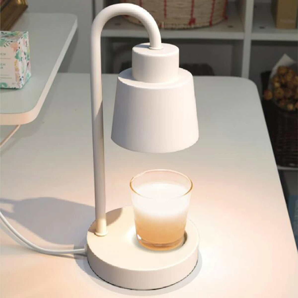 Candle warmer lamp in white with curved neck and base on desk beside a lit candle