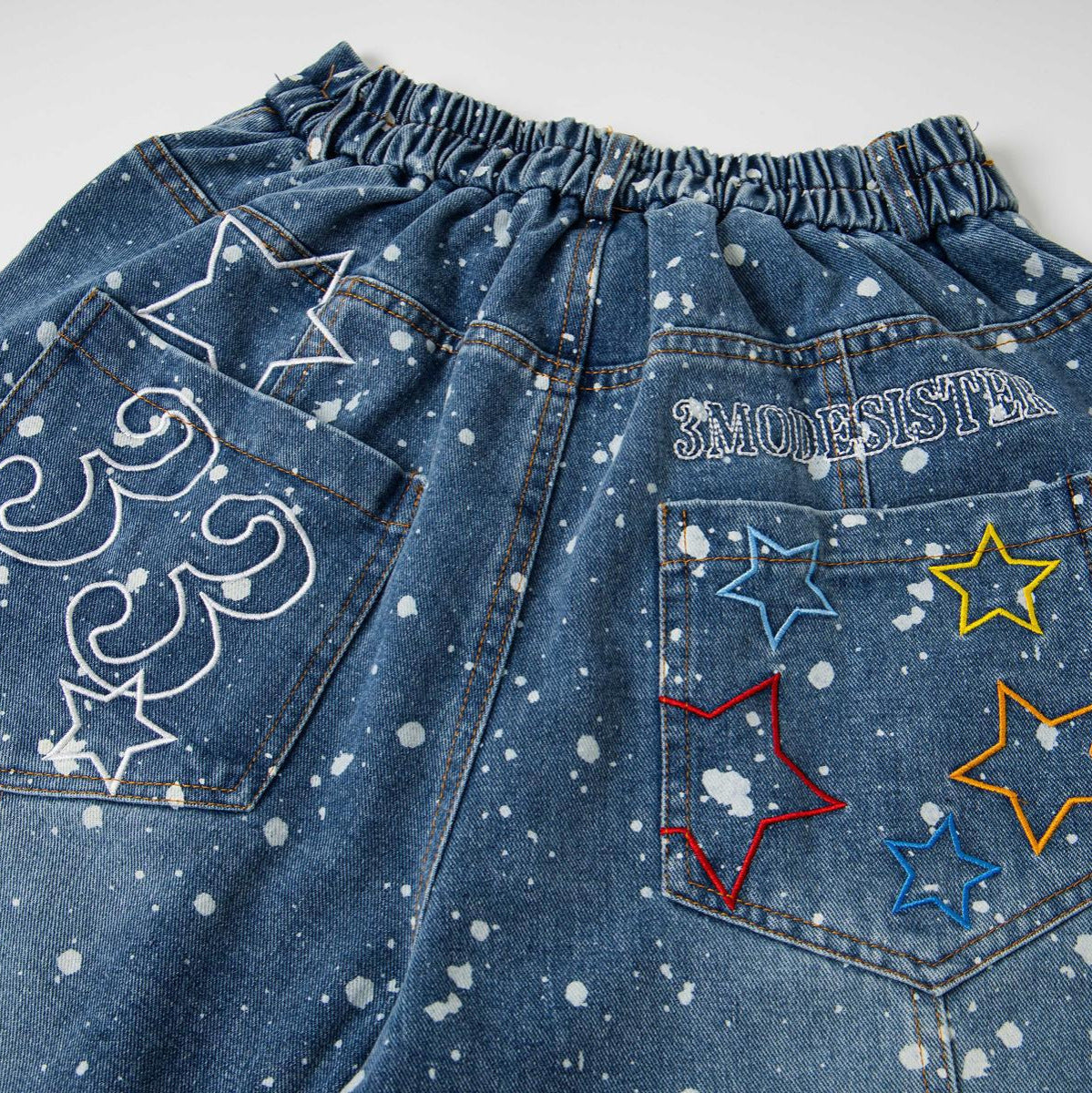 Jeans in blue denim with white paint splatters and colorful star embroidery on back pockets, elastic waistband