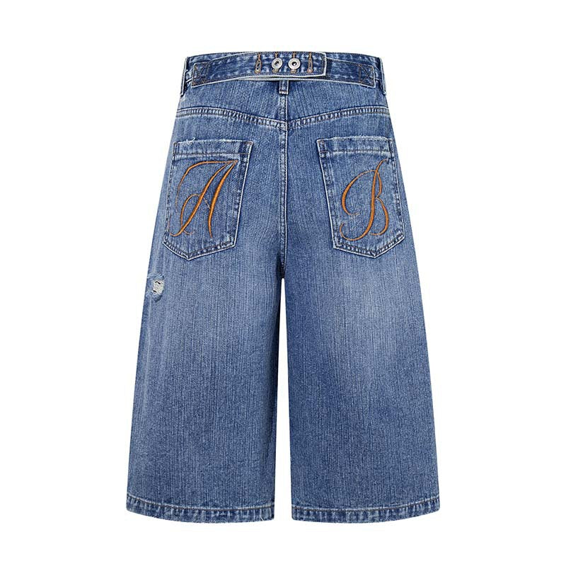 Embroidered blue denim shorts with orange monograms on back pockets and distressed wash