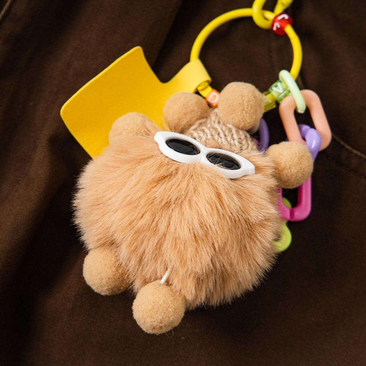 Brown fluffy cartoon plush keychain with white sunglasses and a colorful beaded strap
