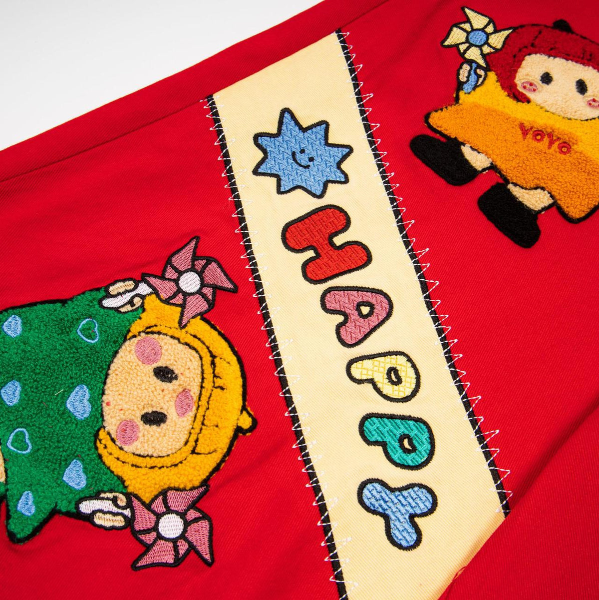 Cartoon plush seven-quarter jeans, red fabric with colorful embroidered characters and a beige striped panel