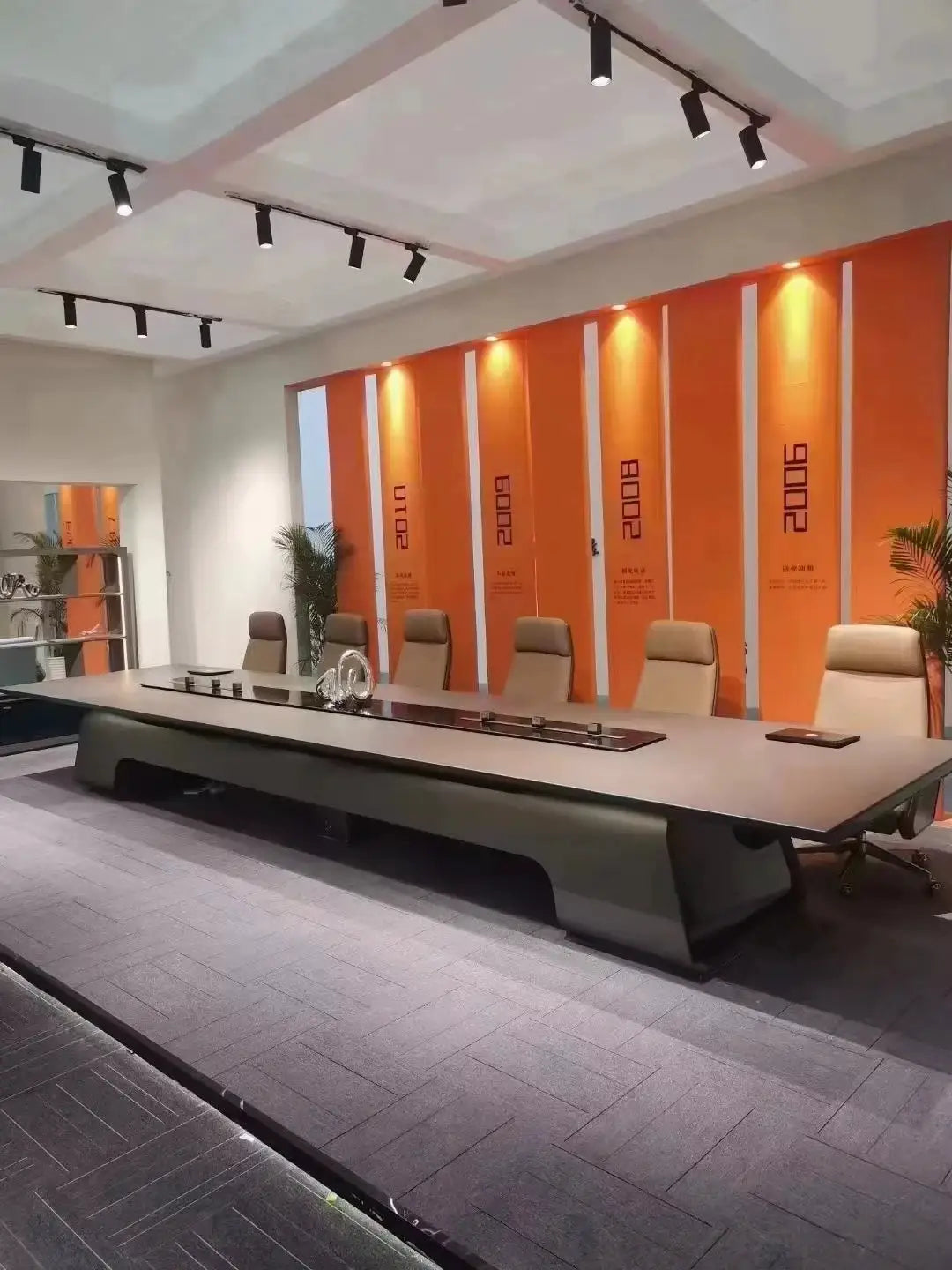 Large executive conference table in a modern rectangular boardroom with beige high-back chairs and orange wall panels.
