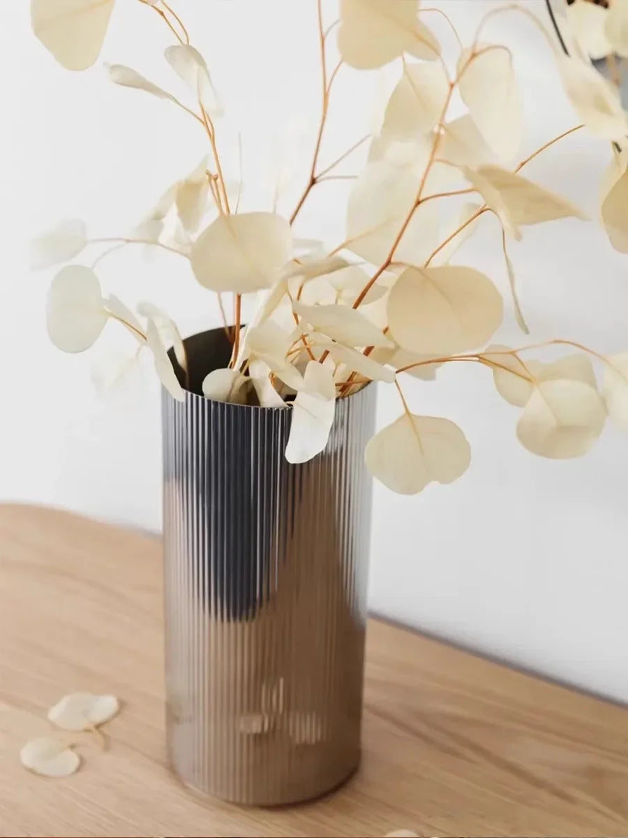 Scandinavian designer stainless steel vase with vertical ridges and bronze-silver finish, holding dried eucalyptus.