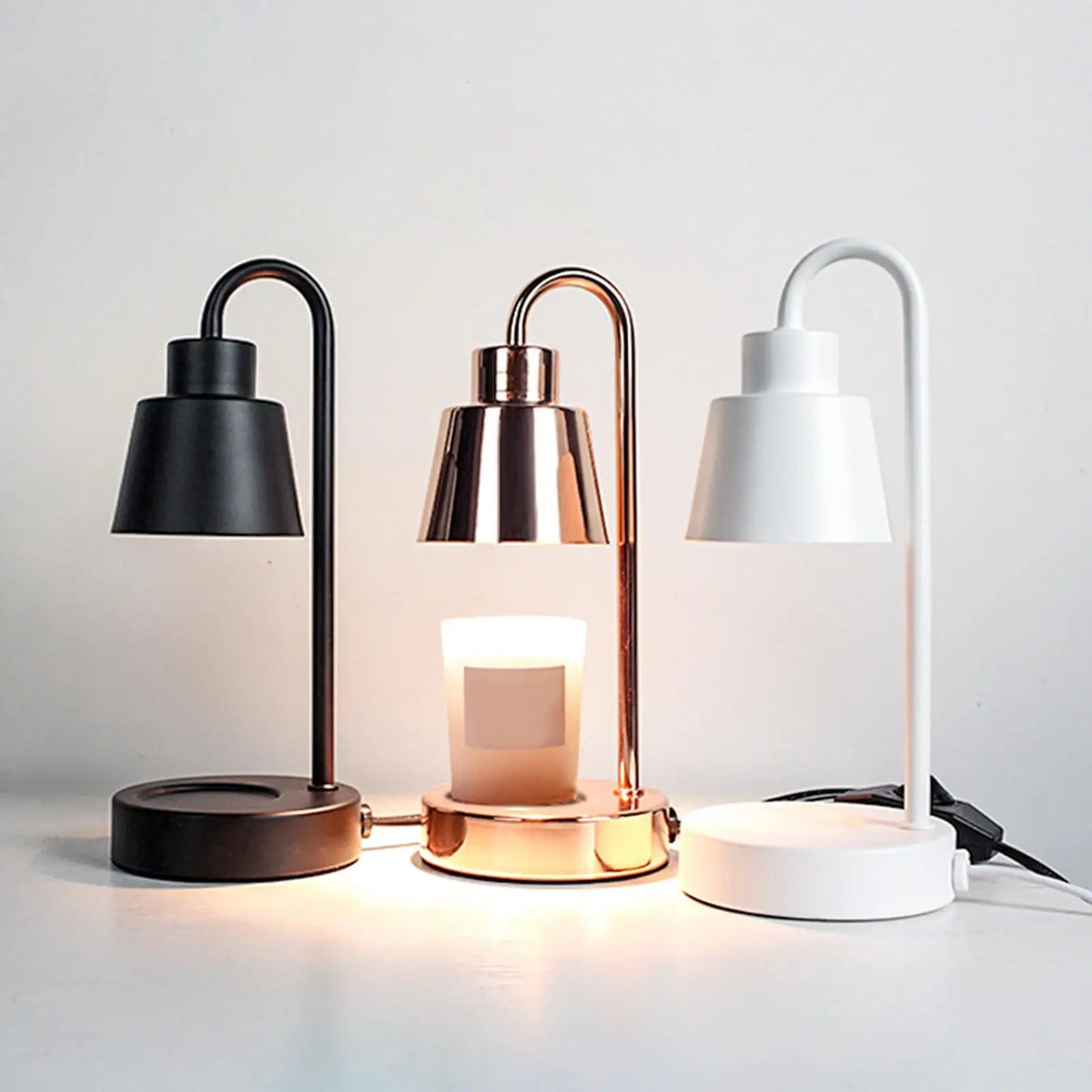 Candle warmer lamp trio in black, rose-gold and white finishes on a round base
