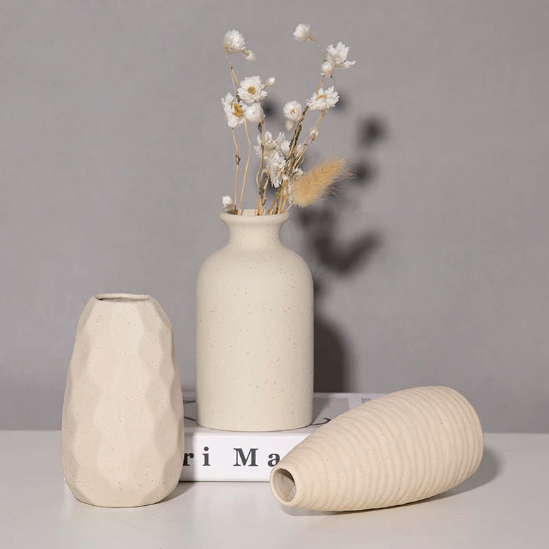 Ceramic vase set of three in beige; tall smooth vase with dried flowers, a faceted geometric vase, and a ribbed elongated vase.