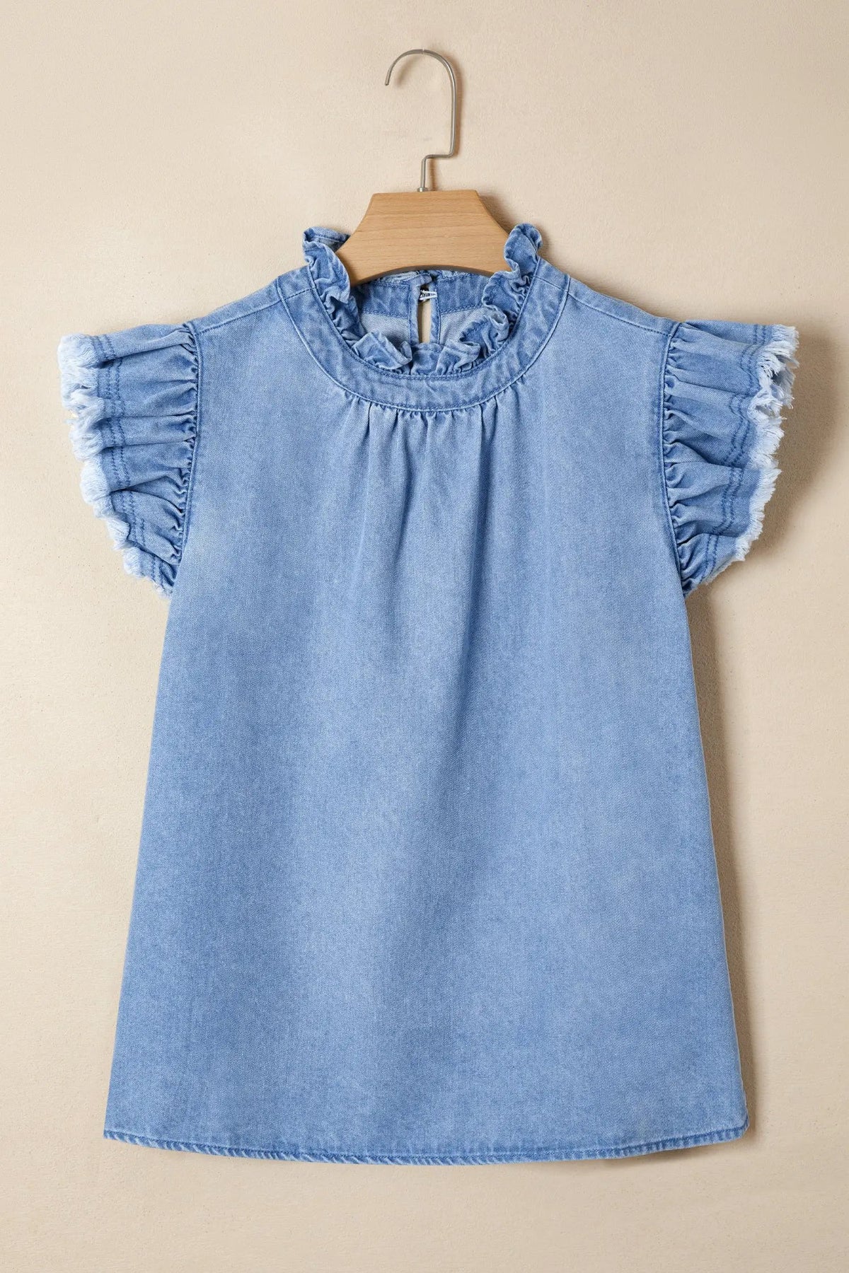 Denim top with frill collar and wide flutter sleeves in light blue, hung on a wooden hanger