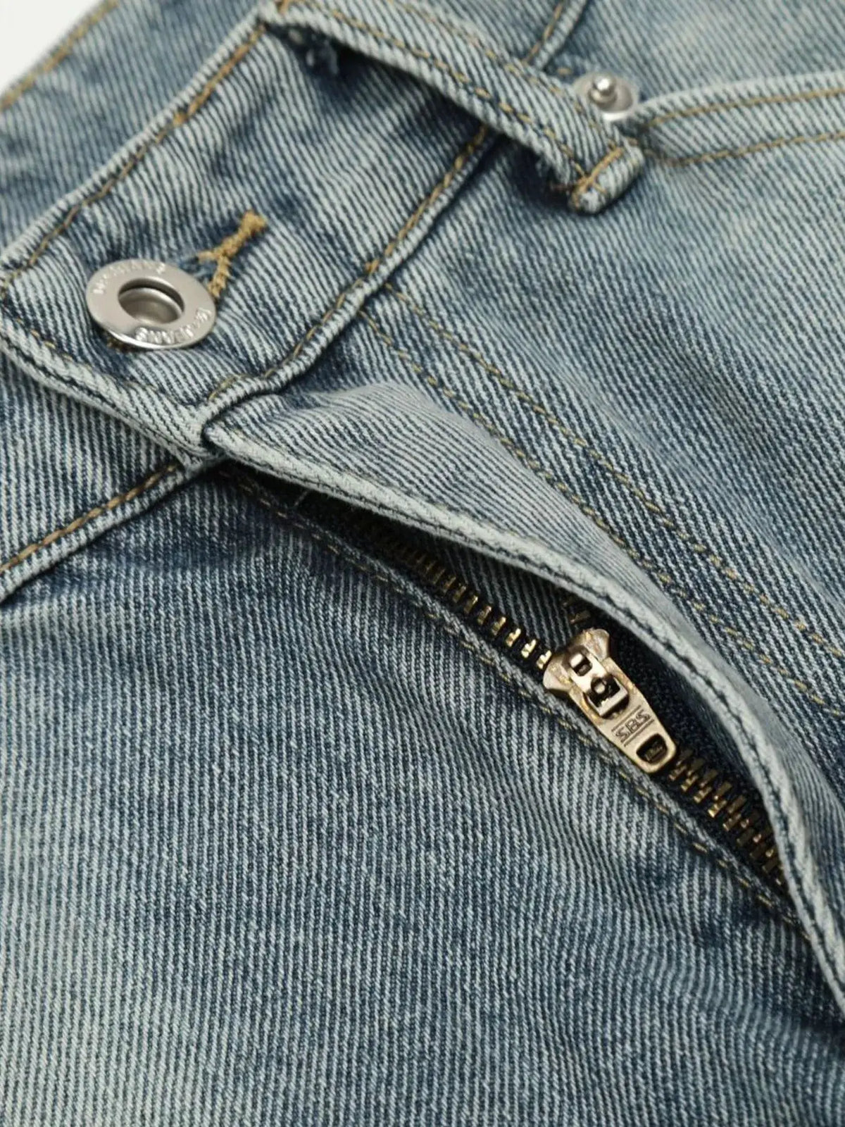 Men's denim shorts close-up showing blue washed denim fabric, metal top button, and exposed zipper with yellow stitching.