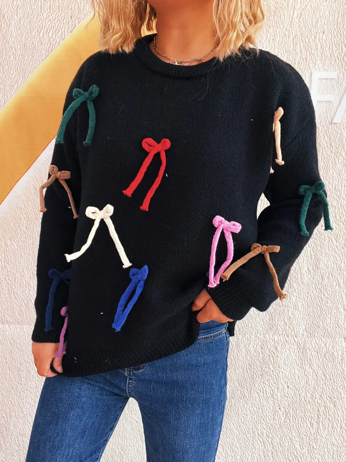 Sweater for women with black knit, round-neck, featuring multicolor bow accents on sleeves and front