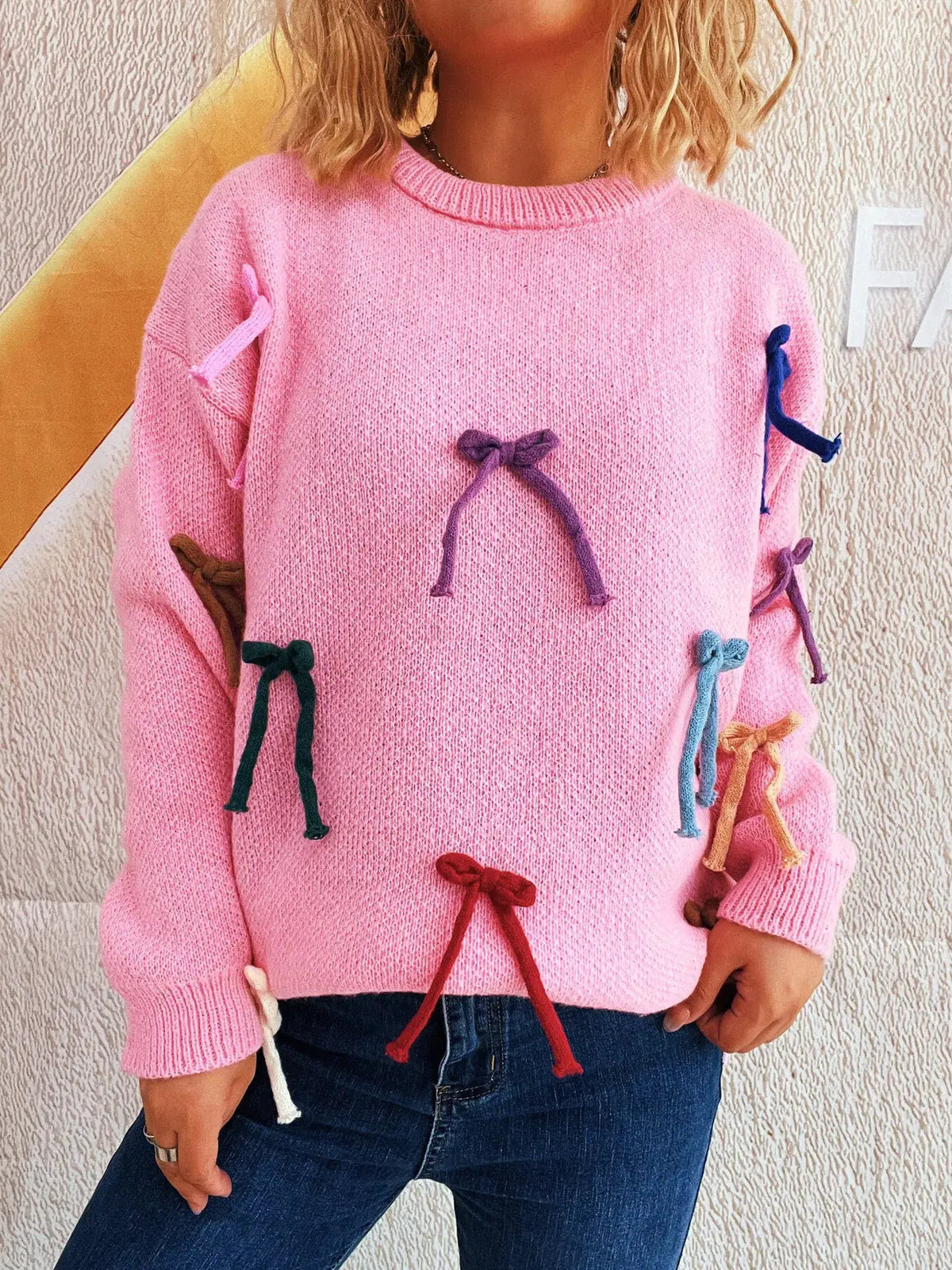 Pink knit sweater for women with multicolor bow accents along front and sleeves, round neck.