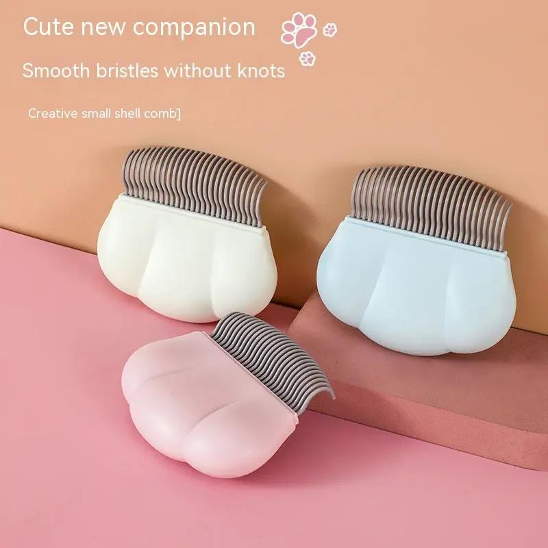 Three pastel shell-style dog grooming combs with metal teeth in pink, white, and blue.