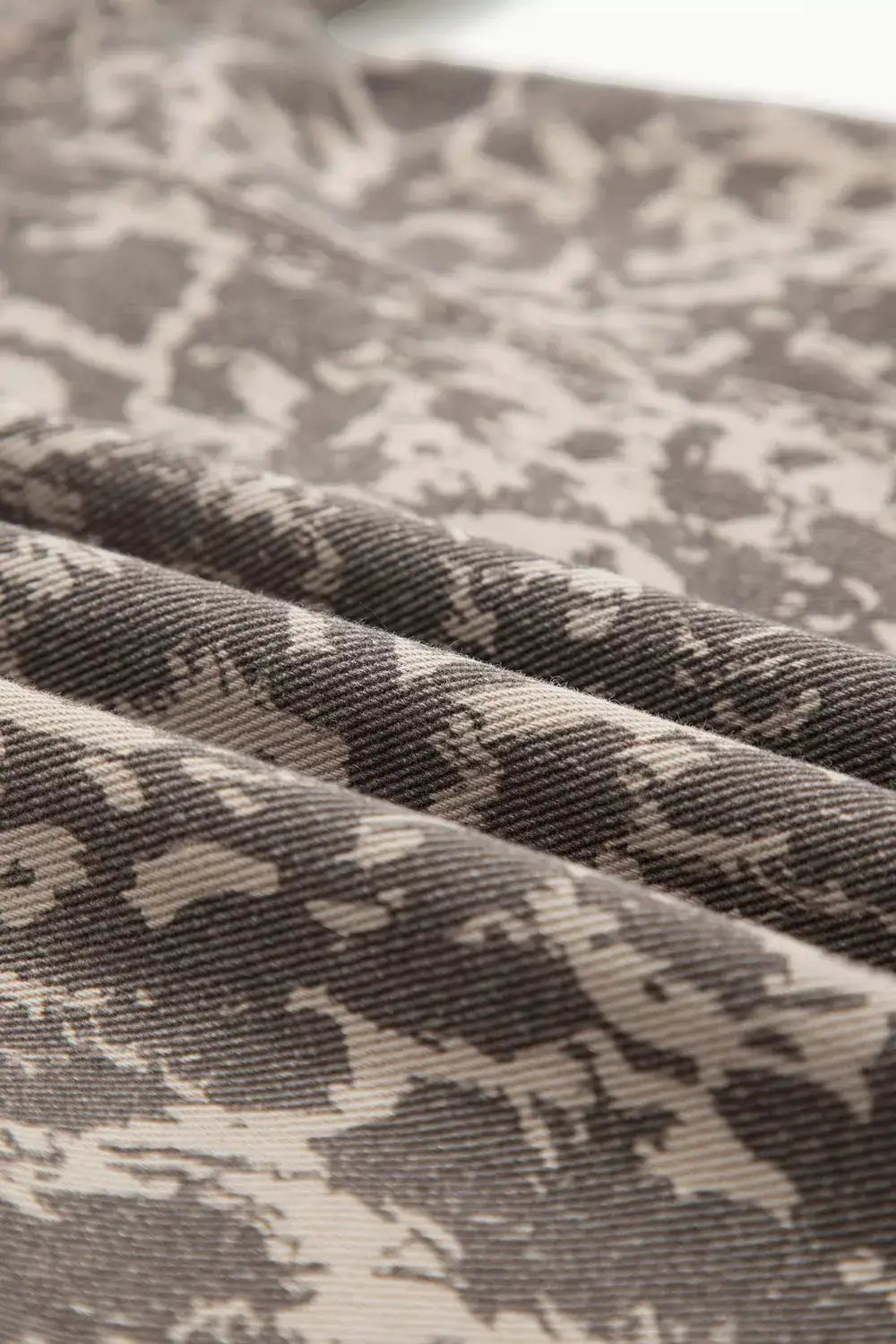 Long-sleeve denim jacket with abstract gray-beige camo print and raw hem.