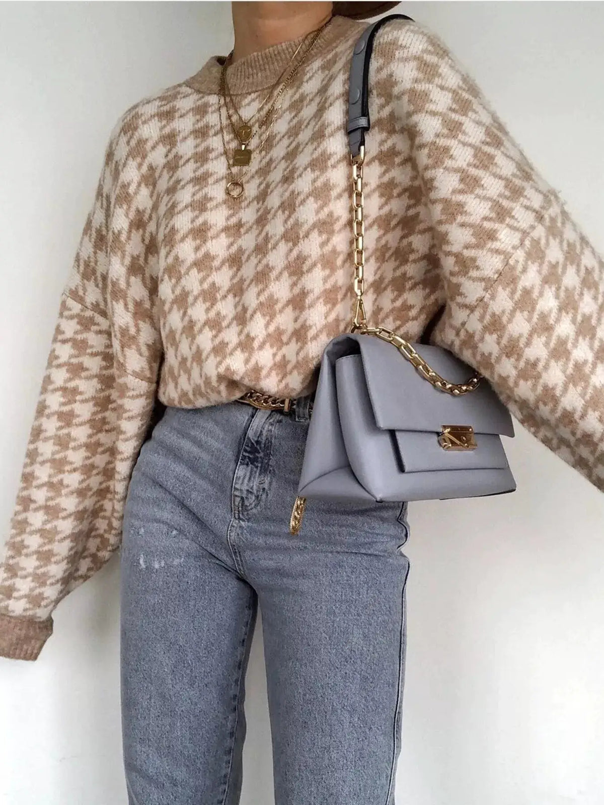 Classic oversized houndstooth sweater in beige/cream; paired with light-wash jeans and a gray handbag with a gold chain.