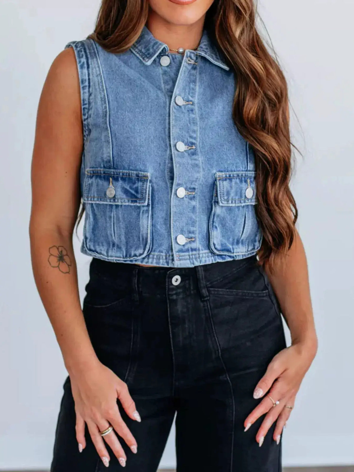 Sleeveless cropped denim vest with button front in light-wash blue, two front pockets.