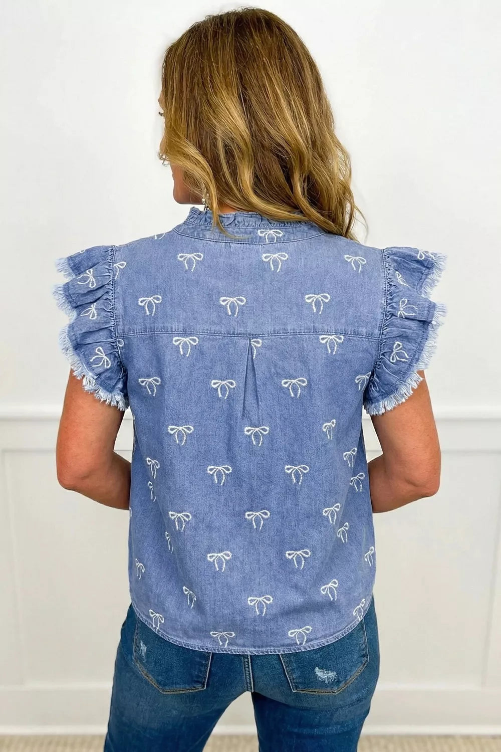 Womens light blue denim top with white bow print, frilled collar, flutter sleeves and raw hem.