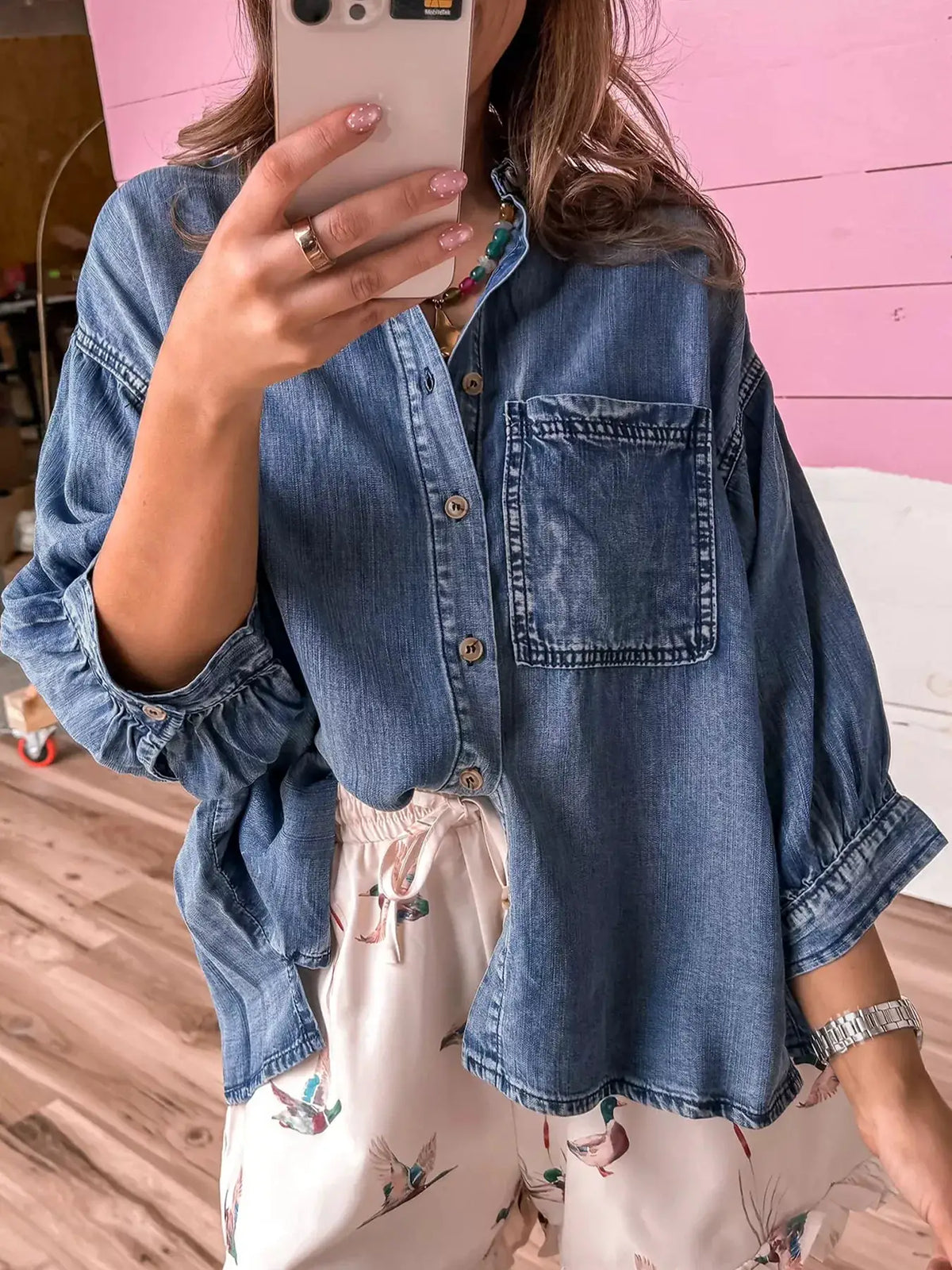 Relaxed denim shirt with three-quarter sleeves and double front pockets, worn over a floral skirt