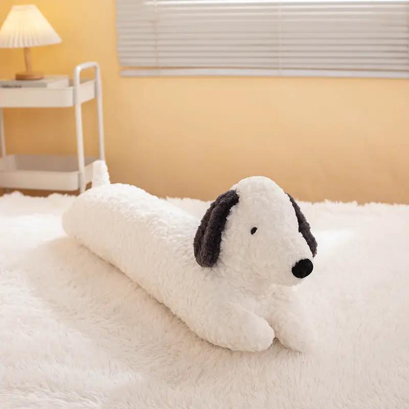 Dachshund plush long pillow doll in white with black ears, resting on a fluffy bed.