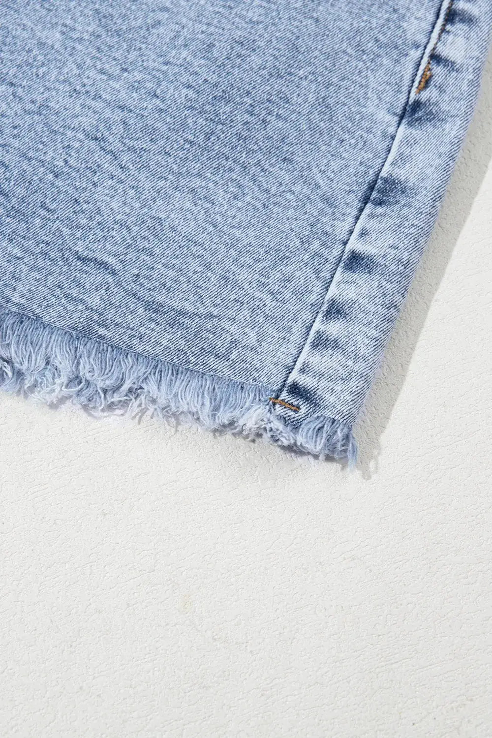 Womens light-wash denim shorts with a frayed raw hem; close-up shows textured fabric.