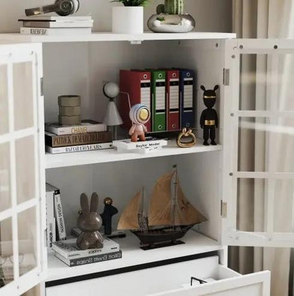 Minimalist white buffet cabinet with double glass doors and drawer, shown with books and a sailboat model.