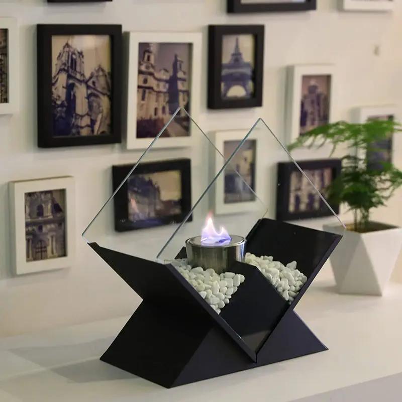 Portable tabletop fireplace with black geometric base, elevated bio-ethanol bowl, glass diamond panels, and white pebbles.