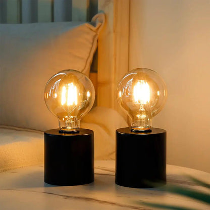 7-inch tall black battery-powered table lamps, set of 2, with clear glass bulbs on a bedside table