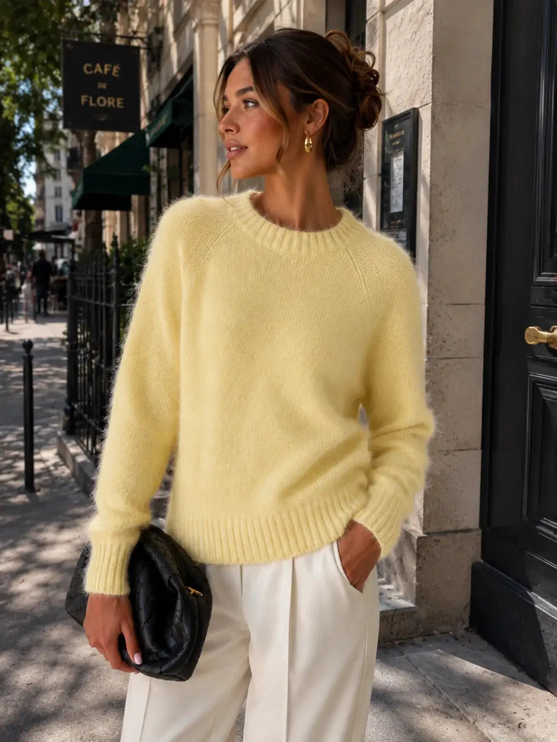 Womens soft cozy knit sweater in pale yellow with fluffy texture, paired with cream trousers and a black quilted clutch.