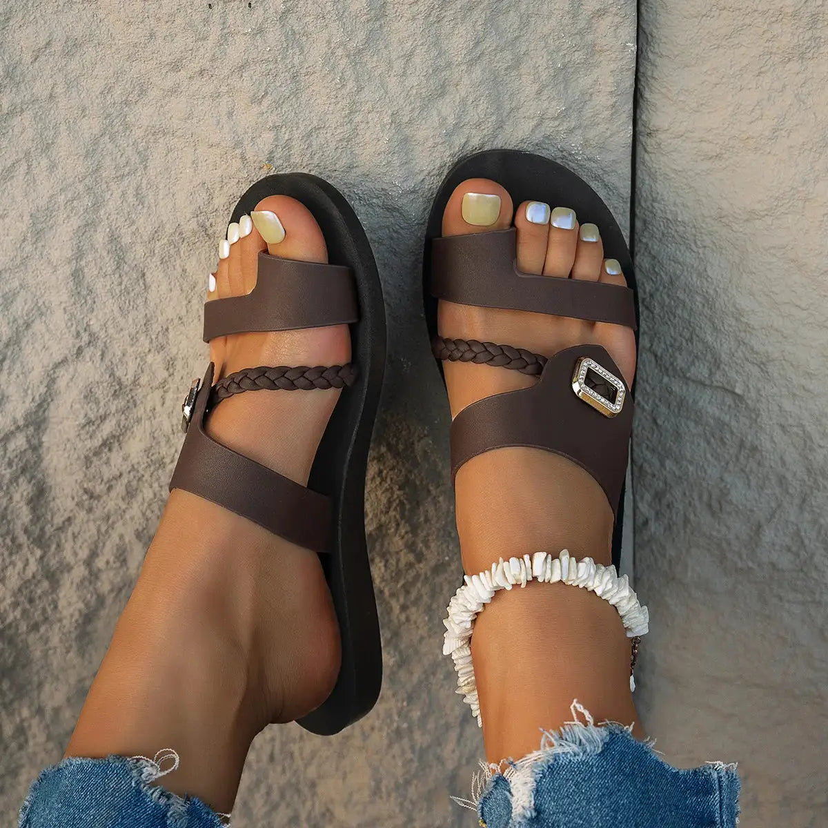 Brown flat sandals with wide toe strap, braided midfoot strap, and rhinestone diamond buckle.