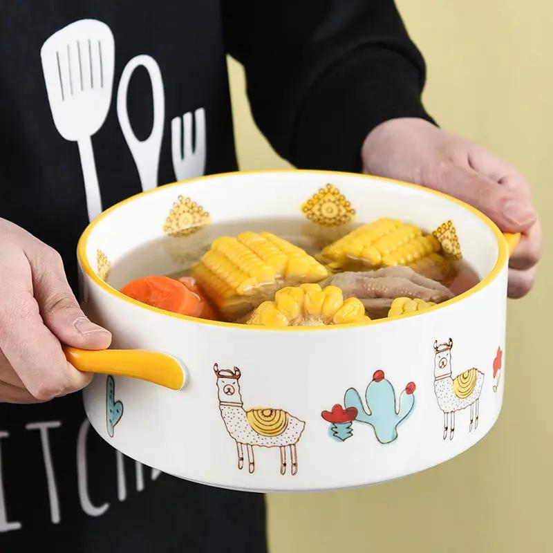 Ceramic double-handled soup bowl with yellow handles, white body with llama and cactus motif, filled with corn and vegetables.