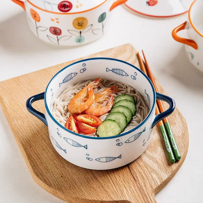 Double-handled ceramic soup bowl with lid, blue rim and fish pattern, filled with noodles, shrimp, cucumber and tomato.
