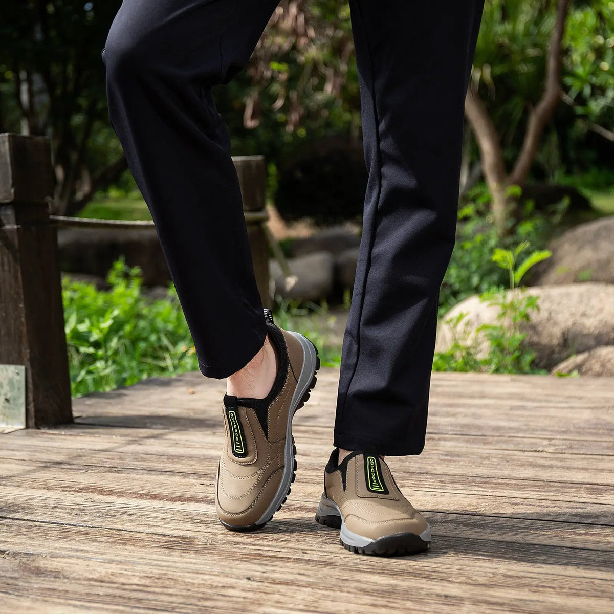 Men's tan outdoor climbing boots, pair shown with rugged lug soles and neon pull-tab on a wooden boardwalk.